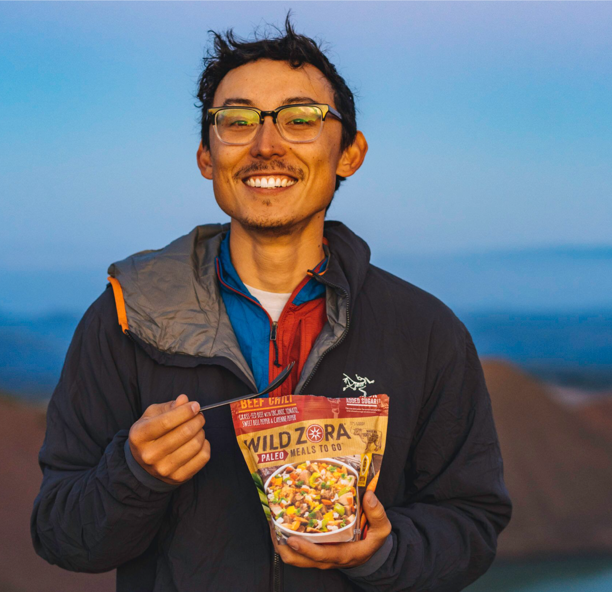 A man holding and eating Wild Zora Bedrock Beef Chili 3 oz freeze-dried meal.
